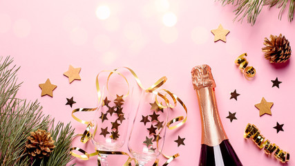 Two champagne flutes with confetti and streamers, champagne bottle in pink and gold colors, copy space. Festive composition for Christmas or New Year. Creative Christmas card on pastel pink background
