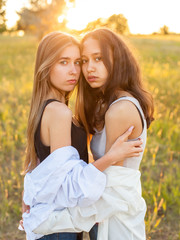 Two girls in white shirts standing together under sunset light. Best friends