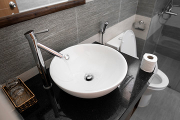 Bathroom interior with white round sink and chrome faucet in a modern bathroom. Water flowing from the chrome faucet.