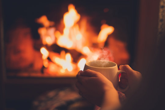 Cup of tea in woman's hands sitting near fireplace