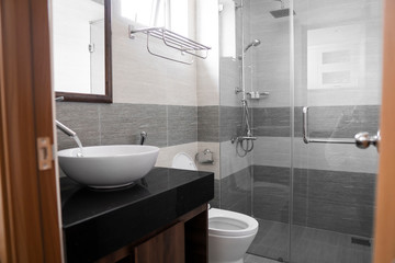 Bathroom interior with white round sink and chrome faucet in a modern bathroom with a toilet and shower. Water flowing from the chrome faucet.