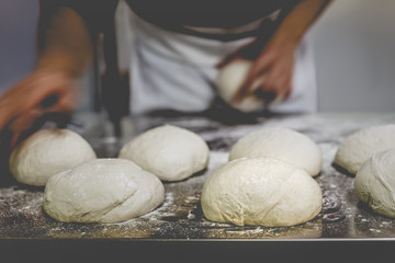 Ball of pizza dough on cooking table with chef in background.