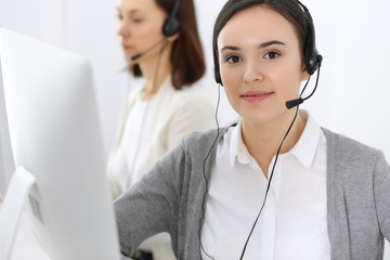 Call center. Beautiful woman receptionist sitting in headset at customer service office. Group of operators at work. Business concept