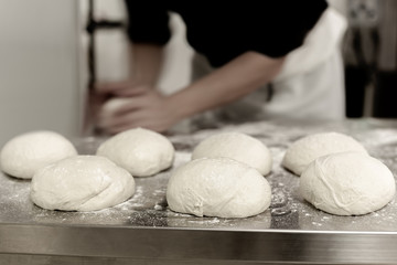 ball of pizza dough on cooking table with chef in background.