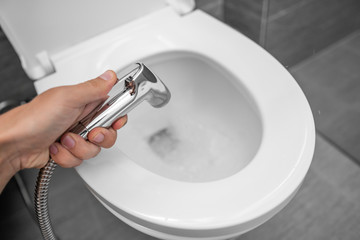 Using of bidet shower with a white toilet. Bidet shower in male hand for using with a white toilet bowl.