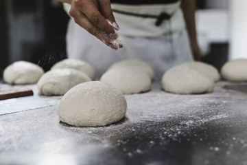 Chef in a kitchen prepares the dough with flour to make a pizza