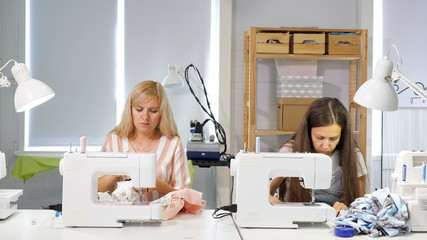 Tailoring of clothes. Seamstresses at work in workshop sewing clothes on sewing machine....
