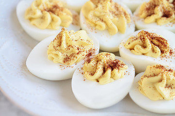 Plate of delicious deviled eggs appetizers sprinkled with paprika for Easter. Selective focus on center front egg with extreme blurred foreground and background. 