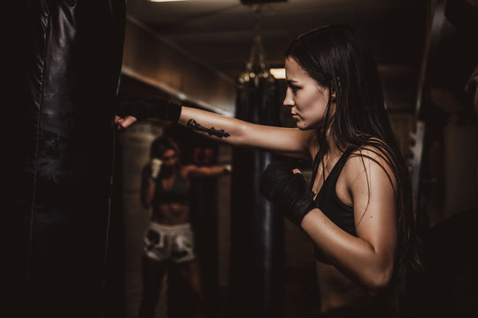 Dark photo of young pretty woman in dark gym, which has a training using punching bag.