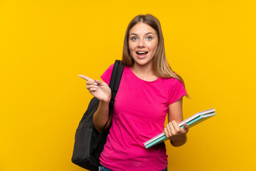 Young student girl over isolated yellow background surprised and pointing finger to the side