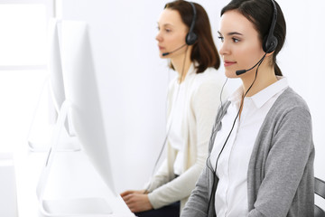 Call center. Beautiful woman receptionist sitting in headset at customer service office. Group of operators at work. Business concept