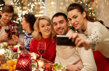 holidays and celebration concept - happy friends having christmas dinner at home and taking selfie by smartphone