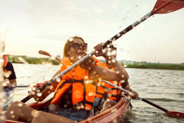 Happy young caucasian group of friends kayaking on river with sunset in the backgrounds. Having fun...