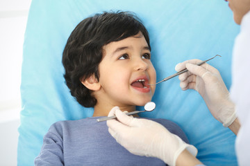 Little arab boy sitting at dental chair with open mouth during oral check up while doctor. Visiting...