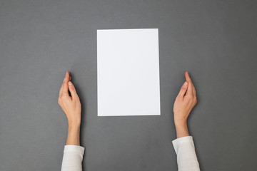 White sheet of paper for your text. Woman holding an empty sheet of paper over gray texture. Overhead view