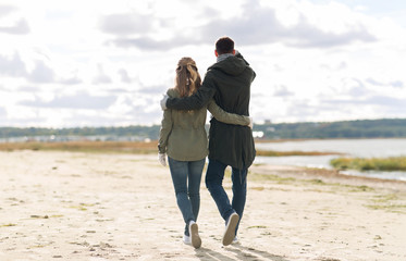 love, relationship and people concept - smiling couple walking along autumn beach and hugging