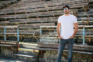 Hipster handsome male model with beard wearing white blank t-shirt and a baseball cap with space for your logo or design in casual urban style