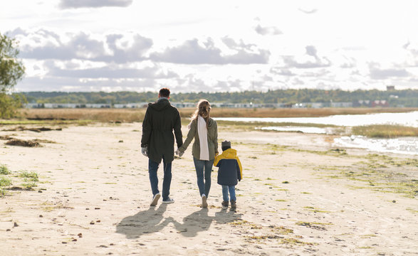 family, leisure and people concept - happy mother, father and little son walking along autumn beach