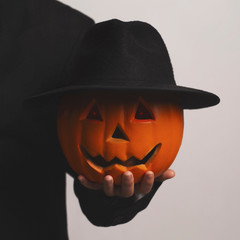 Man holding Halloween serious pumpkin in black hat