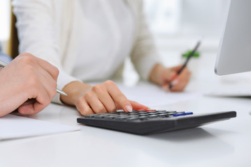 Business woman and man sitting and working with computer and calculator in office, close-up of hands. Bookkeeper or accountant checking balance or making finance report. Tax and audit concepts