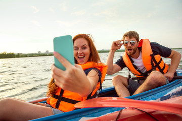 Happy young caucasian couple kayaking on river with sunset in the backgrounds. Having fun in...