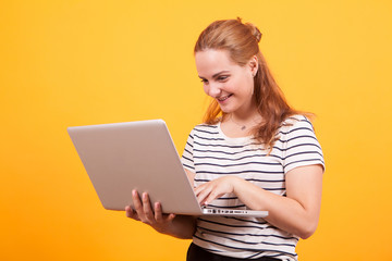 Naklejka premium Girl smiling browsing on laptop in studio over yellow background