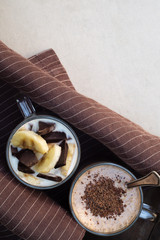 Two glass cups with ingredients banana, chocolate, oatmeal and yogurt smoothie