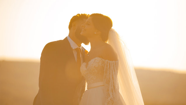 Happty bride is kissed on cheeck by her groom at the sunset.