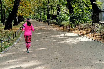 young woman in pink sport clothes running in the park in autumn