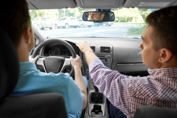 driver courses and people concept - car driving school instructor teaching young man to drive