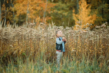 Child boy walks in a glade at the autumn forest.