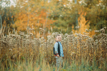 Child boy walks in a glade at the autumn forest.
