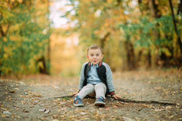 A child boy sits on a pathway in autumn forest.