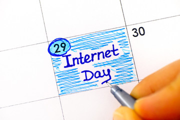 Woman fingers with pen writing reminder Internet Day in calendar.