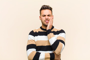 young hispanic man holding cheek and suffering painful toothache, feeling ill, miserable and...