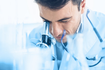 Young scientist look through microscope while doing research in scientific laboratory. Health and...