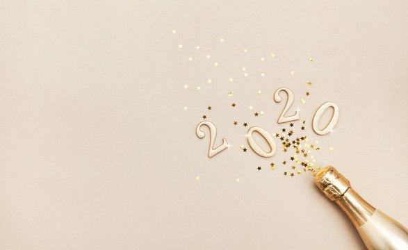 Creative Christmas and New Year composition with golden champagne bottle, confetti stars and 2020 numbers. Flat lay.