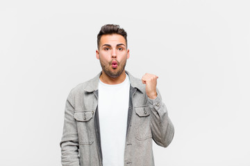 young hispanic man looking astonished in disbelief, pointing at object on the side and saying wow,...