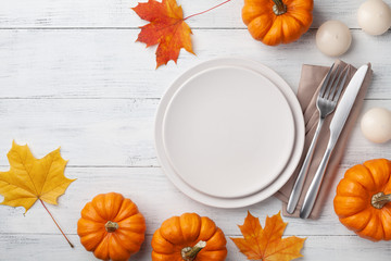 Autumn Thanksgiving table setting for dinner with plate, knife, fork decorated pumpkins and maple...