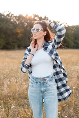 Young woman in plaid shirt and sunglasses walking outdoors.