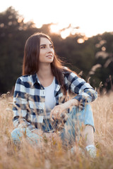 Young beautiful woman in plaid shirt sitting in grass outdoors
