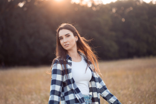 Beautiful young woman in plaid shirt walking outdoors at sunset