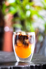 Iced fresh orange juice topped with espresso on wooden table in a garden; as sunrise coffee make a good day.