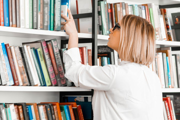 Young attractive pensive woman drawing hand to a book in a book store or library. Woman is on...