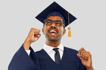 education, graduation and people concept - happy smiling indian male graduate student in mortar...