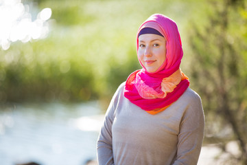 Attractive confident woman in hijab standing outdoors in sunny summer day, happily smiling. Muslim woman lifestyle concept