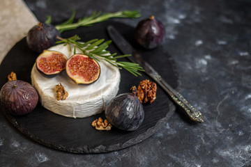 Ripe, beautiful, purple figs.  Sweet and juicy.  Mediterranean fruit is very healthy.  On a plate is Brie cheese.  There is empty space on a dark copyspace background.  Food for vegetarians.