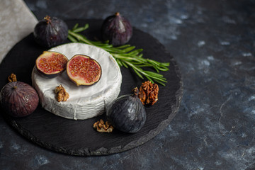 Ripe, beautiful, purple figs.  Sweet and juicy.  Mediterranean fruit is very healthy.  On a plate is Brie cheese.  There is empty space on a dark copyspace background.  Food for vegetarians.