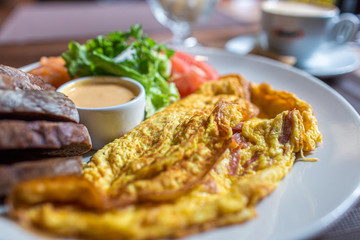 Fresh omelette served with green salad, tomatoes. sause and breab - close up view. Cup of coffee on a background. Traditional breakfast. Healthy food.