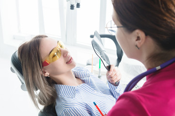 Dentist woman doctor talking to a young patient sitting on the dentist chair in a medical office. The first conversation with the client and external visual inspection